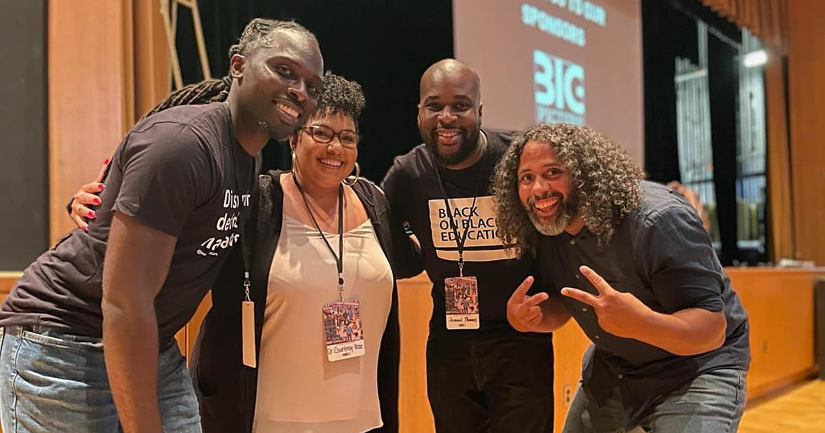 Four Black educators standing in front of a stage at the HipHopEd Conference