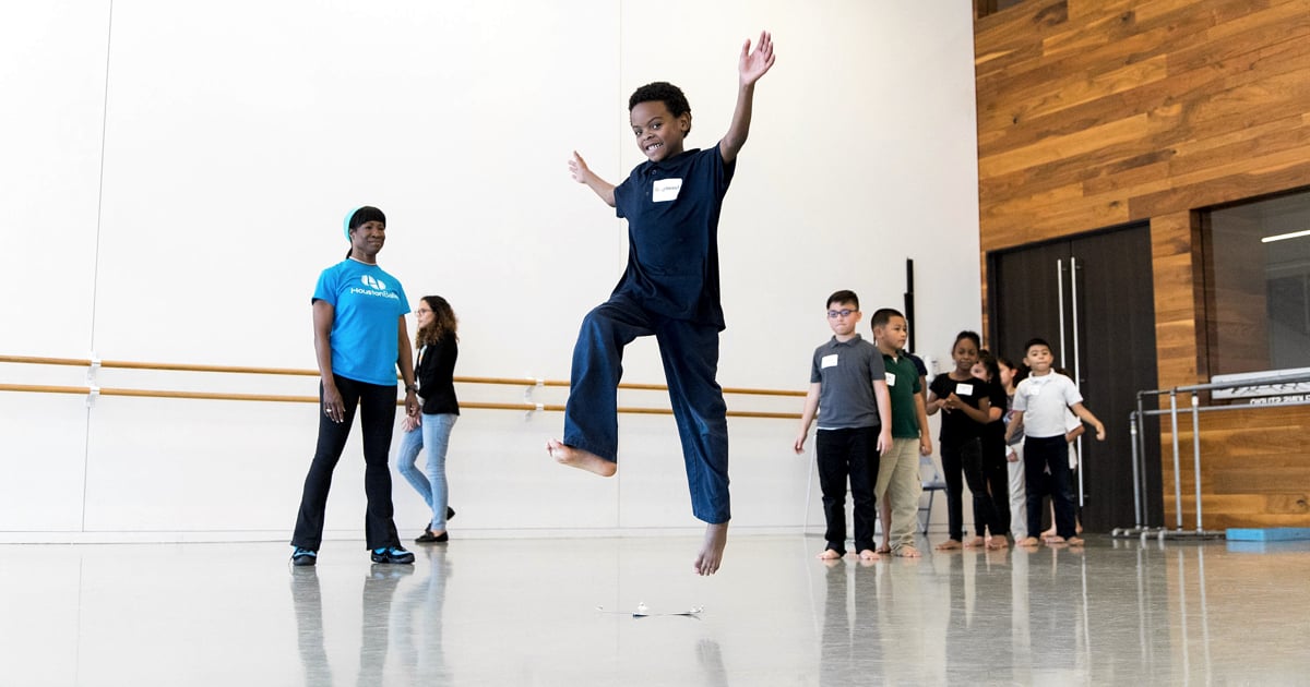 Houston Ballet Chance to Dance Program, Young Black boy leaping in the air with a line of diverse students behind him