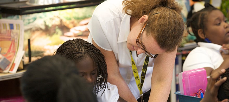 A white teacher looking over the shoulder of a Black student