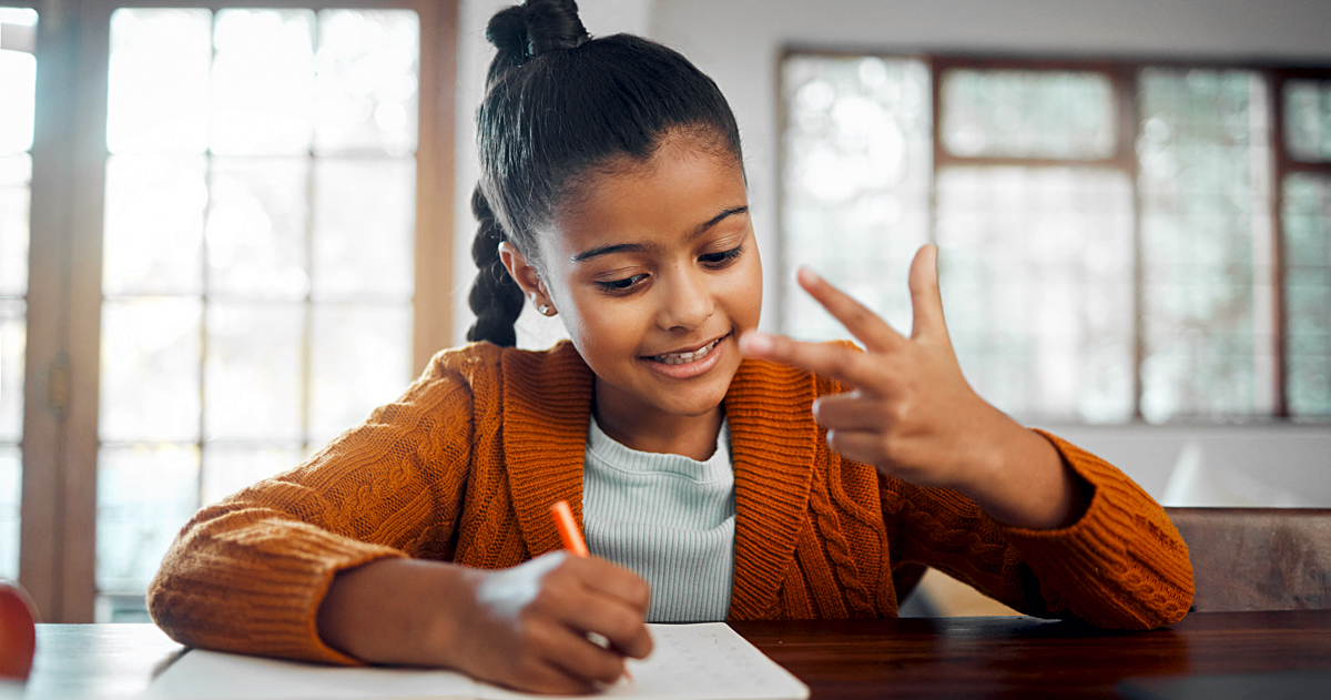Young Black girl sitting at a desk holding a pencil and counting on her fingers.