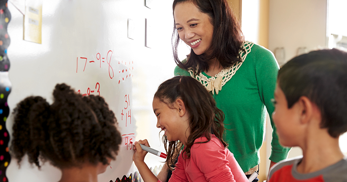 Asian Woman teaching diverse children math on a whiteboard