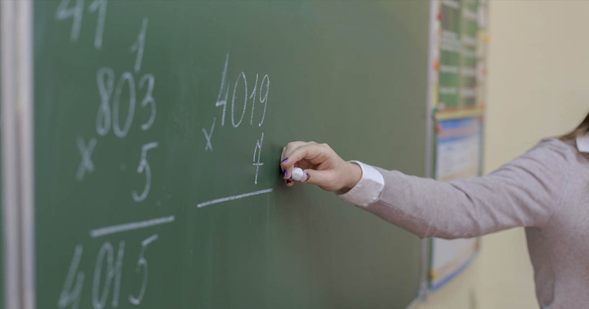 A teacher writes a math equation on a chalkboard